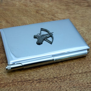 Op de afbeelding: Een zilveren metalen sigarettenkoker met een klein, driedimensionaal boogschutterontwerp aan de voorkant.