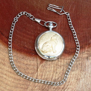 May include: Silver pocket watch with a gold wolf design on the face and a silver chain.