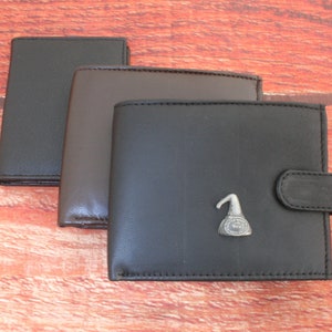 May include: Three leather wallets in black, brown, and dark brown. The largest wallet has a silver metal pin with a design of a hat on it.