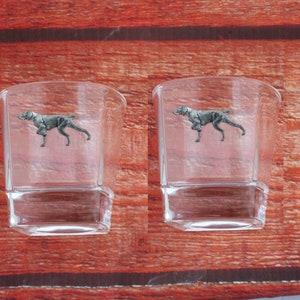 Può includere: Due bicchieri da shot in vetro trasparente con un design di cane Bracco tedesco a pelo corto argentato sul davanti.