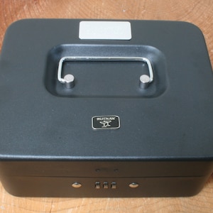 May include: A black metal cash box with a combination lock and a silver handle. The box has a silver label that says "SECURITY" on it.