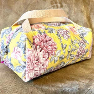 May include: A yellow floral print fabric tote bag with a cream colored handle. The bag has a zipper closure and a pink floral design.