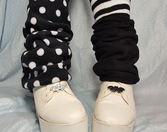 Può includere: Un paio di scarpe platform bianche con gambali neri e bianchi. Un gambale ha un motivo a pois e l'altro ha strisce nere e bianche. Ogni scarpa ha un ciondolo a forma di pipistrello nero sui lacci.