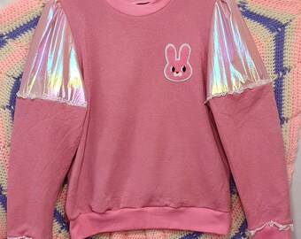 May include: Pink sweatshirt with iridescent sleeves and a pink bunny applique. The sleeves have a white lace trim.