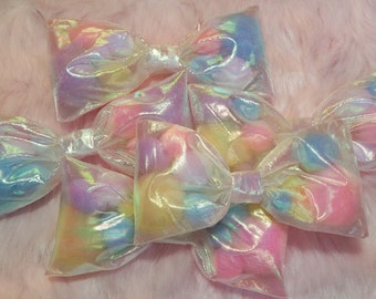 May include: A set of five iridescent pastel-colored bows made of sheer fabric. The bows are tied together and have a delicate, feminine look.