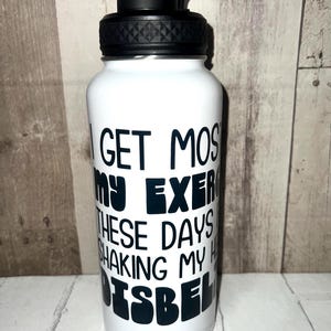 May include: White water bottle with a black lid and handle. The bottle has the text "I GET MOST OF MY EXERCISE THESE DAYS SHAKING MY HEAD ISBEL" in black lettering. The bottle is cylindrical and appears to be made of metal.