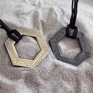 May include: Two necklaces with hexagonal pendants. One pendant is gold with a geometric design and the other is black with a similar design.