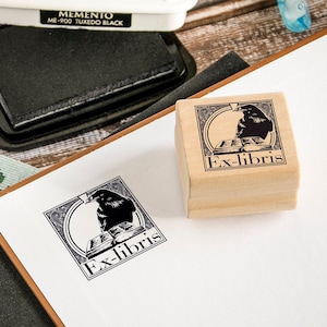 May include: Two wooden stamps with a black and white illustration of a raven and the text "Ex-libris". The stamps are on a white surface.