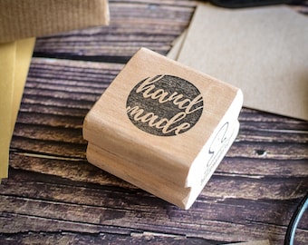 Könnte beinhalten: Ein Stempel aus Holz mit einem schwarzen Kreis und dem Text "hand made" im Kreis.