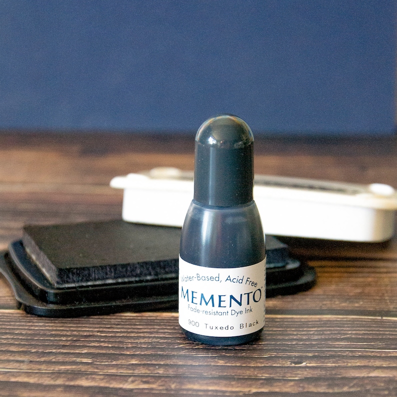 May include: A black ink bottle with a label that reads "Water-Based, Acid Free MEMENTO Fade-resistant Dye Ink 300 Tuxedo Black".