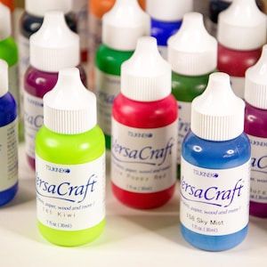 K&ouml;nnte beinhalten: Eine Sammlung von 30 ml Flaschen VersaCraft Alkohol-Tinten in verschiedenen Farben, darunter Blau, Gr&uuml;n, Rot, Lila und Burgunder. Die Flaschen haben wei&szlig;e Verschl&uuml;sse und sind mit dem Markennamen und dem Farbnamen beschriftet.