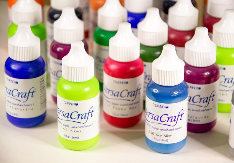 K&ouml;nnte beinhalten: Eine Sammlung von 30 ml Flaschen VersaCraft Alkohol-Tinten in verschiedenen Farben, darunter Blau, Gr&uuml;n, Rot, Lila und Burgunder. Die Flaschen haben wei&szlig;e Verschl&uuml;sse und sind mit dem Markennamen und dem Farbnamen beschriftet.