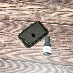 May include: A black ink pad with a small hole in the center and a black bottle of ink labeled "Memento" on a wooden surface.