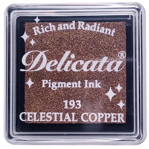 May include: A square ink pad with a metallic copper color. The ink pad is labeled "Delicata Pigment Ink" and "Celestial Copper" with the number "193". The ink pad is in a clear plastic case.