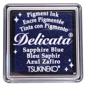 May include: A clear plastic container with a black ink pad inside. The ink pad is blue and says "Delicata Sapphire Blue Bleu Saphir Azul Zafiro TSUKINEKO" in white lettering.