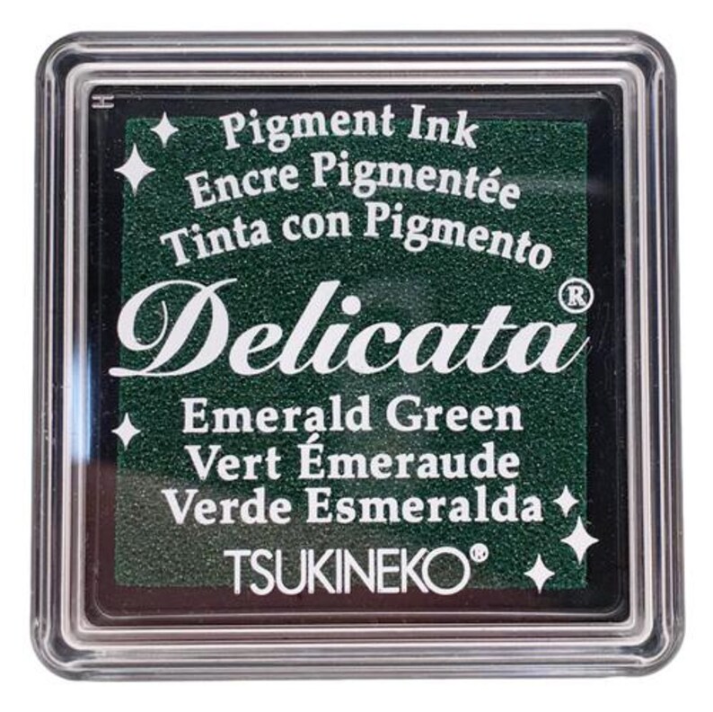May include: A green ink pad with the text "Pigment Ink", "Encre Pigment&eacute;e", "Tinta con Pigmento", "Delicata", "Emerald Green", "Vert &Eacute;meraude", "Verde Esmeralda", and "TSUKINEKO&reg;".