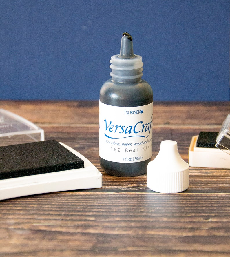 K&ouml;nnte beinhalten: Eine schwarze Tintenflasche mit der Aufschrift "VersaCraft" von Tsukineko. Die Flasche ist 1 Fl&uuml;ssigunze (30 ml) gro&szlig; und f&uuml;r Stoff, Papier, Holz und mehr geeignet.
