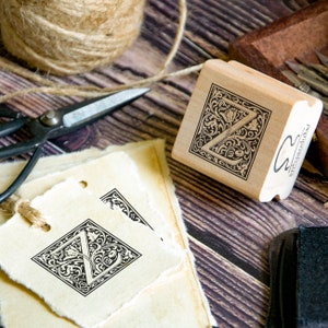 May include: A wooden stamp with a decorative design featuring the letter "Z" in a square frame. The stamp is made by "Artpark Ink".
