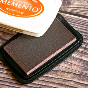 May include: A brown ink pad with the text "Memento" and "Potter's Clay" on the lid. The ink pad is in a black plastic case.