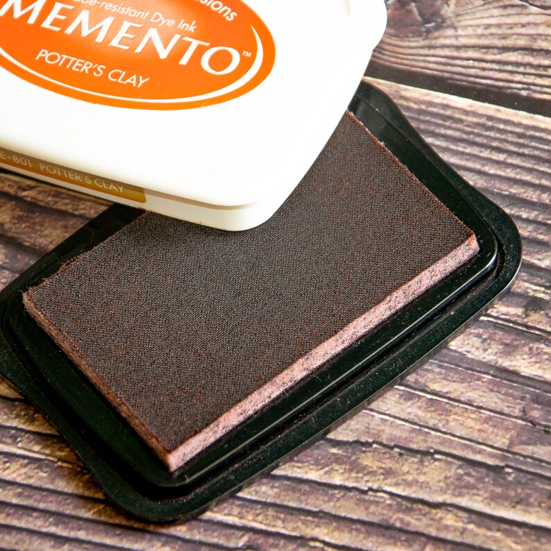 May include: A brown ink pad with the text "Memento" and "Potter's Clay" on the lid. The ink pad is in a black plastic case.