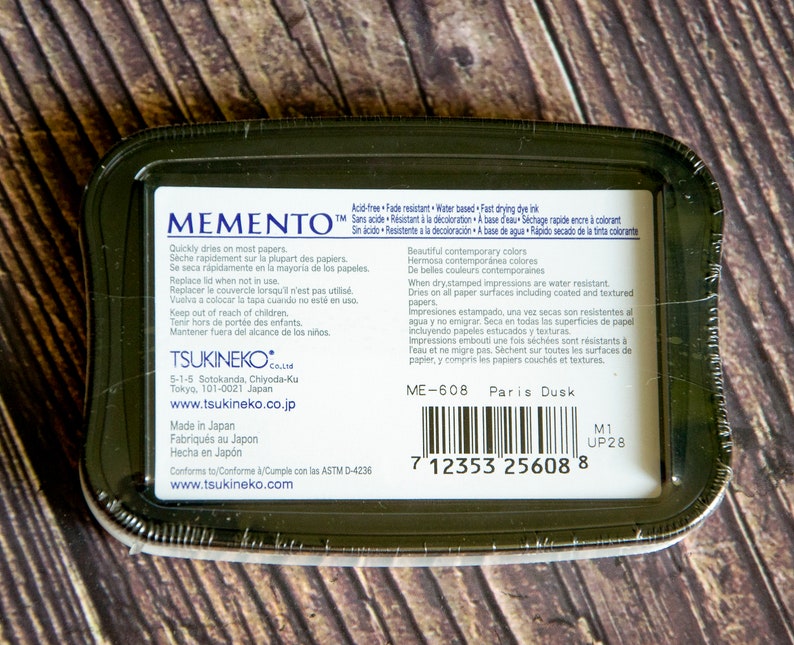 May include: Memento Paris Dusk dye ink pad, acid-free, fade resistant, water-based, fast drying, and dries on most papers. The ink pad is packaged in a black plastic container with a barcode and the text "ME-608 Paris Dusk".