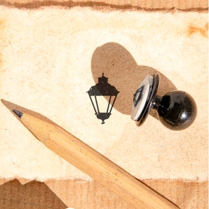 May include: A black rubber stamp with a streetlight design on a brown paper background. A wooden pencil is lying on the paper.