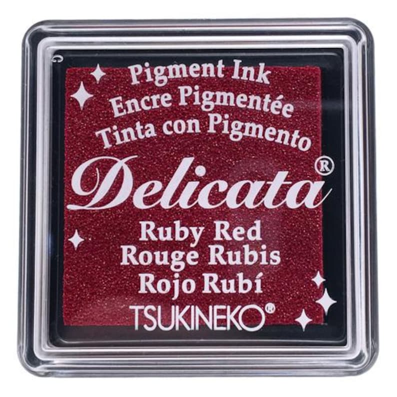 May include: A red ink pad with the text "Pigment Ink", "Encre Pigment&eacute;e", "Tinta con Pigmento", "Delicata", "Ruby Red", "Rouge Rubis", "Rojo Rub&iacute;", and "TSUKINEKO&reg;".