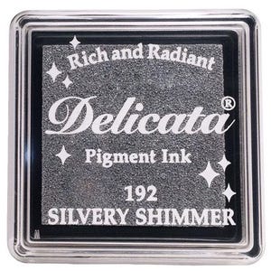 May include: A silver ink pad with the text "Rich and Radiant Delicata Pigment Ink 192 SILVERY SHIMMER" and a small star design.