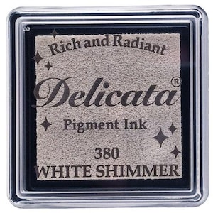 May include: A white shimmer pigment ink pad in a clear plastic case. The ink pad is labeled "Delicata" with the text "Rich and Radiant Pigment Ink 380 White Shimmer".