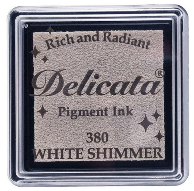 May include: A white shimmer pigment ink pad in a clear plastic case. The ink pad is labeled "Delicata" with the text "Rich and Radiant Pigment Ink 380 White Shimmer".