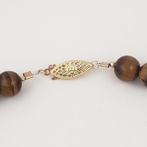 May include: A gold-toned clasp with a delicate filigree design connects two brown tiger's eye beads on a necklace.
