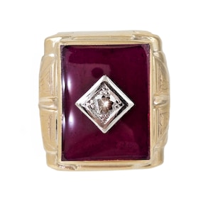 May include: A gold ring with a deep red stone and a small diamond in the center.