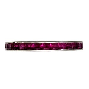 May include: A silver band ring featuring a continuous row of vibrant, rectangular-cut rubies. The gemstones are a deep, rich magenta color, set closely together within the polished metal. The ring's design is simple and elegant.