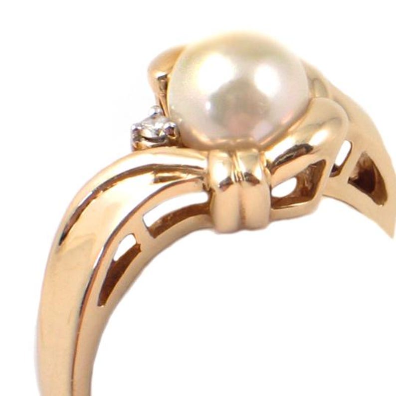 May include: A gold ring with a pearl and a diamond. The ring is designed with a knot-like band.