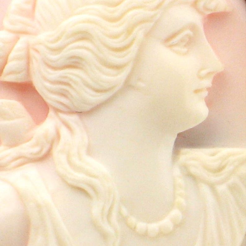 May include: A cameo carving of a woman's face with a pearl necklace. The carving is made of white shell and is set against a pink background.