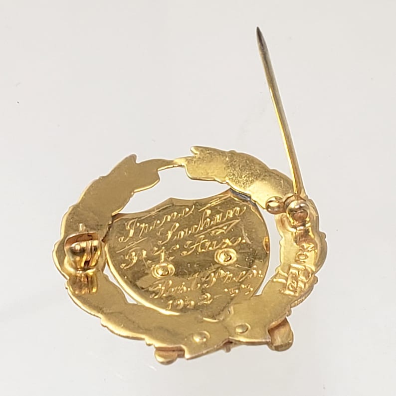 May include: Gold-toned pin with a wreath design and a shield in the center. The shield has the inscription "Irene Southern 1922" and "Paris 1. Prize 1922".