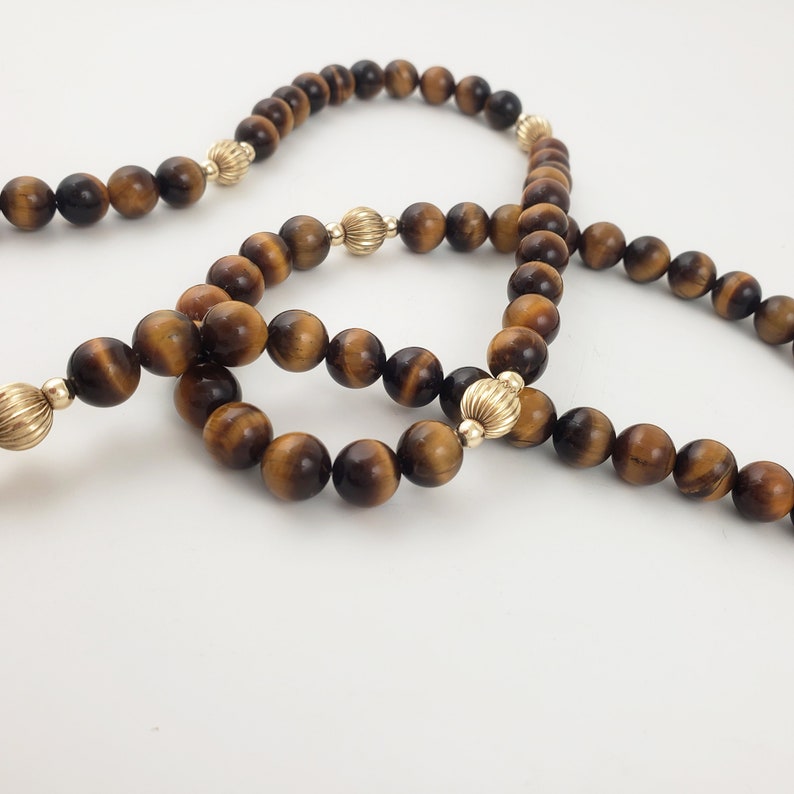 May include: Three strands of tiger's eye beads with gold accents. The beads are brown and gold in color.