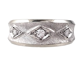 May include: A silver-toned ring with a textured band featuring three diamond-shaped settings, each holding a small, round, clear gemstone. The ring has a polished, smooth edge.