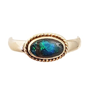 May include: A gold ring with an oval-shaped opal gemstone. The opal is a dark green and black color with flashes of blue and green.