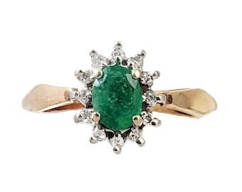 May include: A gold ring with a large oval emerald gemstone surrounded by a halo of smaller diamonds.