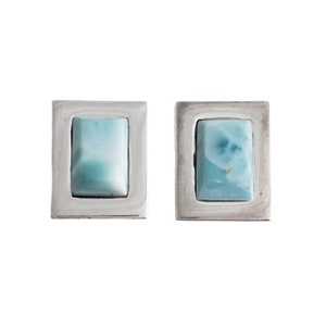 May include: A pair of silver earrings with light blue square-shaped stones set in a silver frame.
