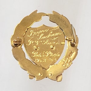 May include: Gold-toned pin with a laurel wreath design. The center features a shield with the inscription "Irene Sorenson, R.V. Aux., Past 1st Pres. 1952-53".