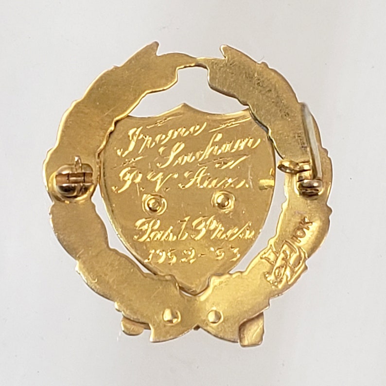 May include: Gold-toned pin with a laurel wreath design. The center features a shield with the inscription "Irene Sorenson, R.V. Aux., Past 1st Pres. 1952-53".