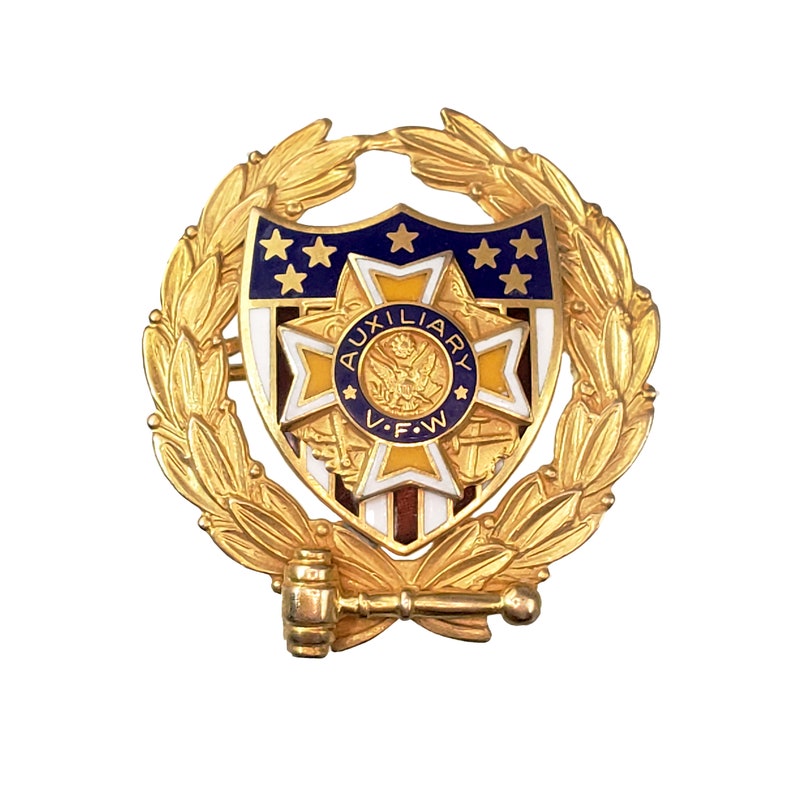 May include: Gold-toned pin with a shield-shaped design featuring a blue and white American flag, a yellow star, and the text "AUXILIARY V.F.W." surrounded by a gold laurel wreath. A gold gavel is attached to the bottom of the pin.