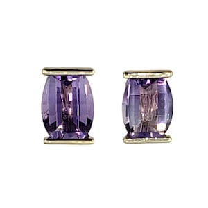 May include: A pair of stud earrings featuring faceted, barrel-shaped purple gemstones. The gemstones are set in a gold-colored metal setting, creating a striking contrast. The earrings are displayed against a white background.