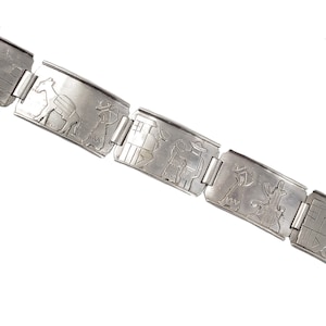 May include: A silver bracelet with a repeating pattern of engraved figures. The figures depict people and animals in a traditional style.