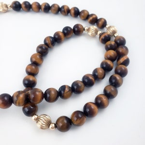 May include: A double strand necklace made of brown tiger's eye beads with gold accents.