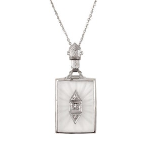 May include: A silver chain necklace with a rectangular pendant featuring a carved crystal with a diamond-shaped design and three small diamonds.