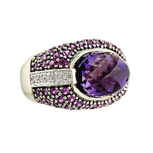 May include: A gold ring with a large purple amethyst gemstone surrounded by smaller pink gemstones. The ring is set in a gold band.