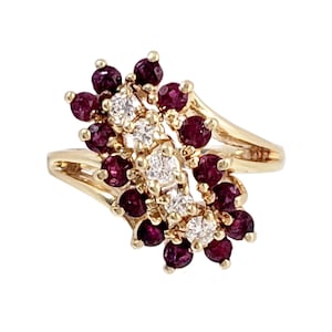 May include: A gold ring with a cluster of red rubies and diamonds. The ring is set in a delicate, swirling design.